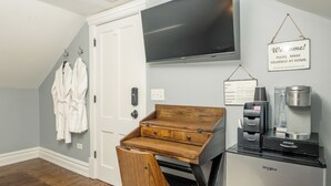 Ett rum med ett skrivbord i trä, en stol, en kaffebryggare, ett kylskåp och en tv som är monterad på väggen.