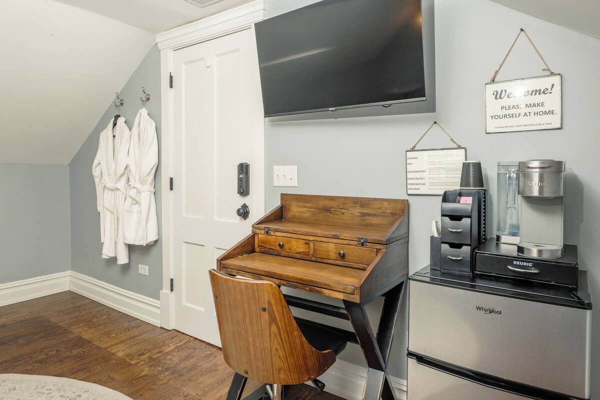 Une pièce comprenant un bureau en bois, une chaise, une machine à café, un réfrigérateur et un téléviseur fixé au mur.