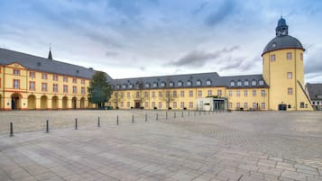 A courtyard with a yellow building featuring a tower and a clock.
