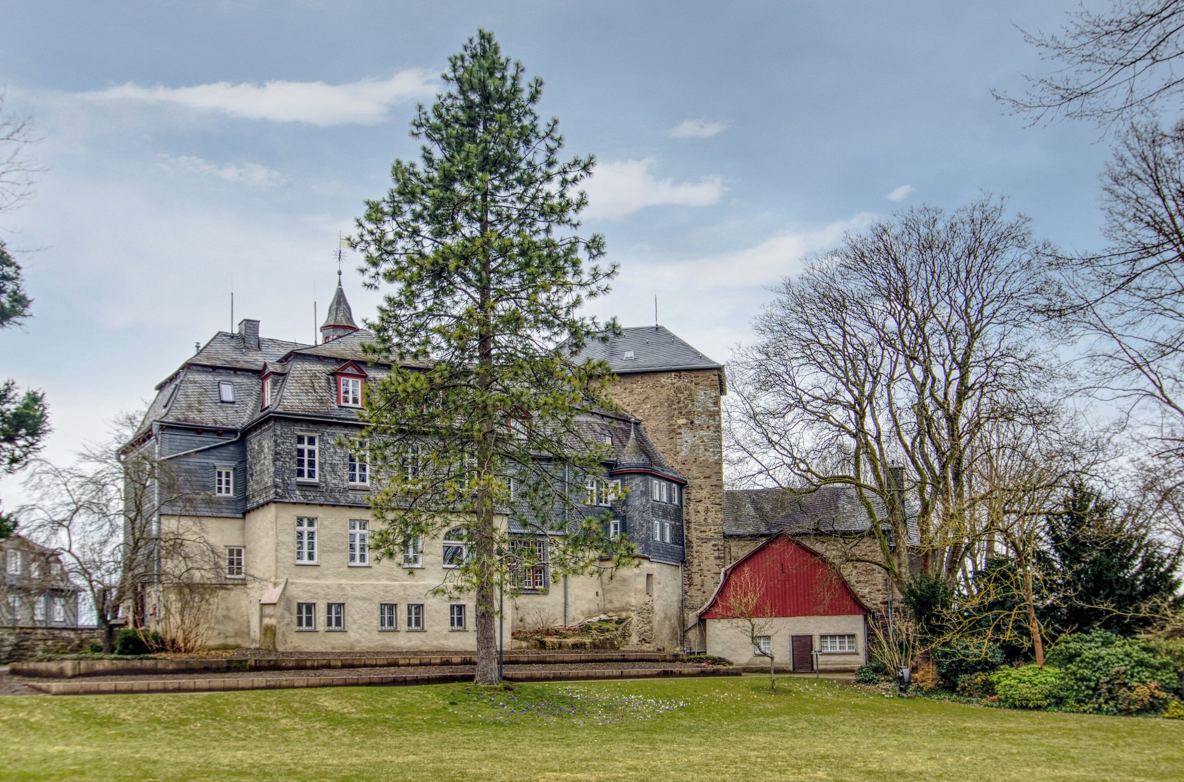 A large, multi-story building with a prominent tower, surrounded by a well-maintained lawn and mature trees.