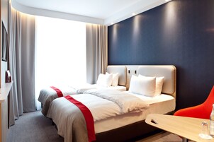 A hotel room with two beds, a desk, and a chair.