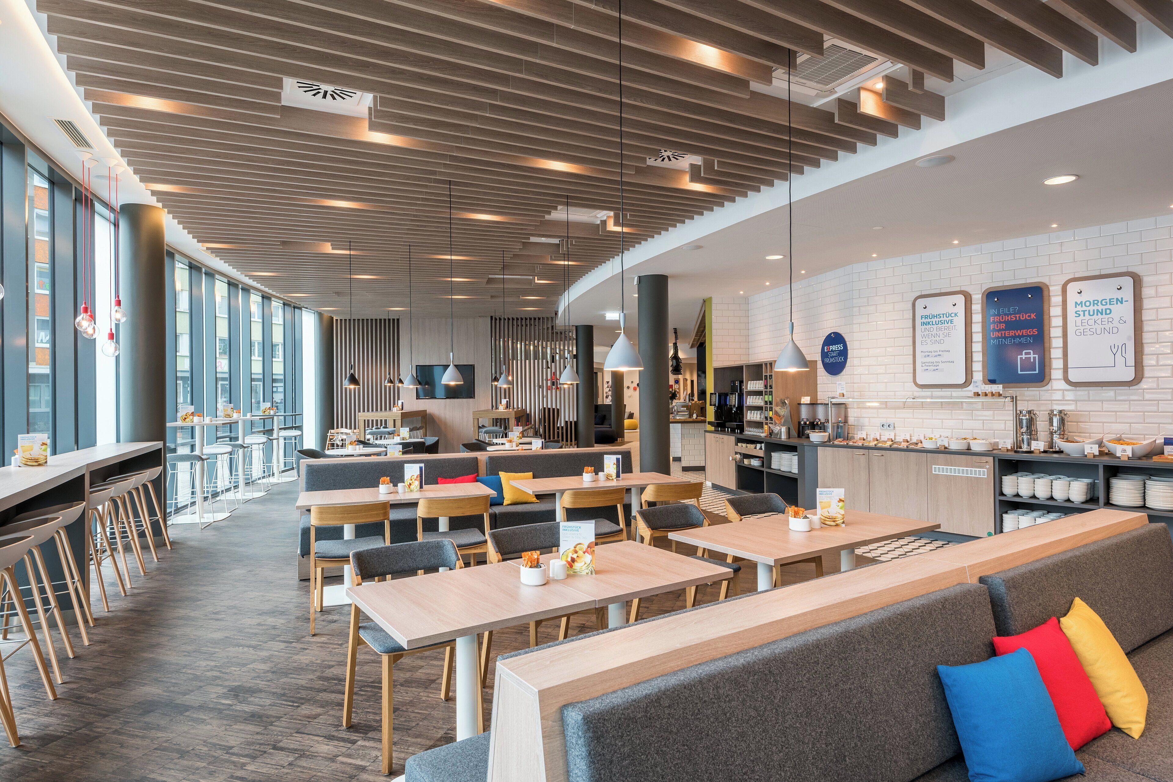 A modern restaurant with a long counter, seating area, and a kitchen in the background.