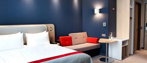 Una habitación de hotel con una cama grande, un sofá, una mesita y un escritorio.