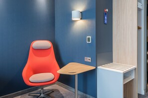 A modern hotel room with a blue accent wall, a red chair, a small wooden table, and a wall-mounted light fixture. - Holiday Inn Express Siegen by IHG (Siegen)