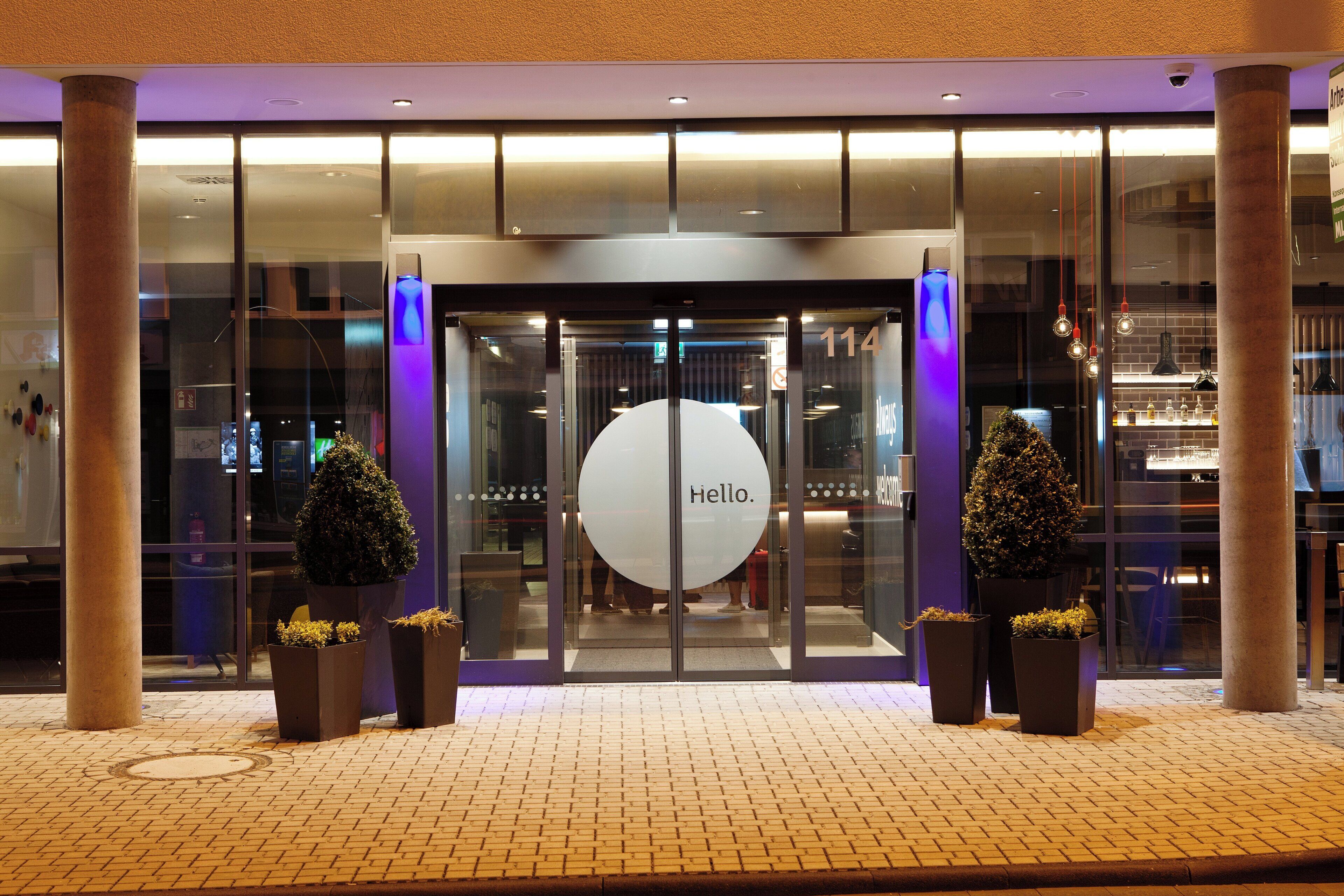Entrada de un hotel con puerta giratoria, puertas de cristal y un letrero que dice 'Hello'.