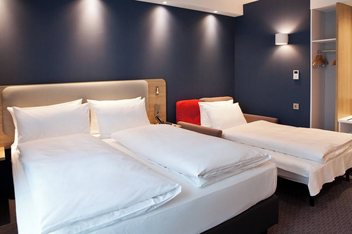 Habitación de hotel con dos camas, cabecera de madera, almohada roja y armario empotrado.