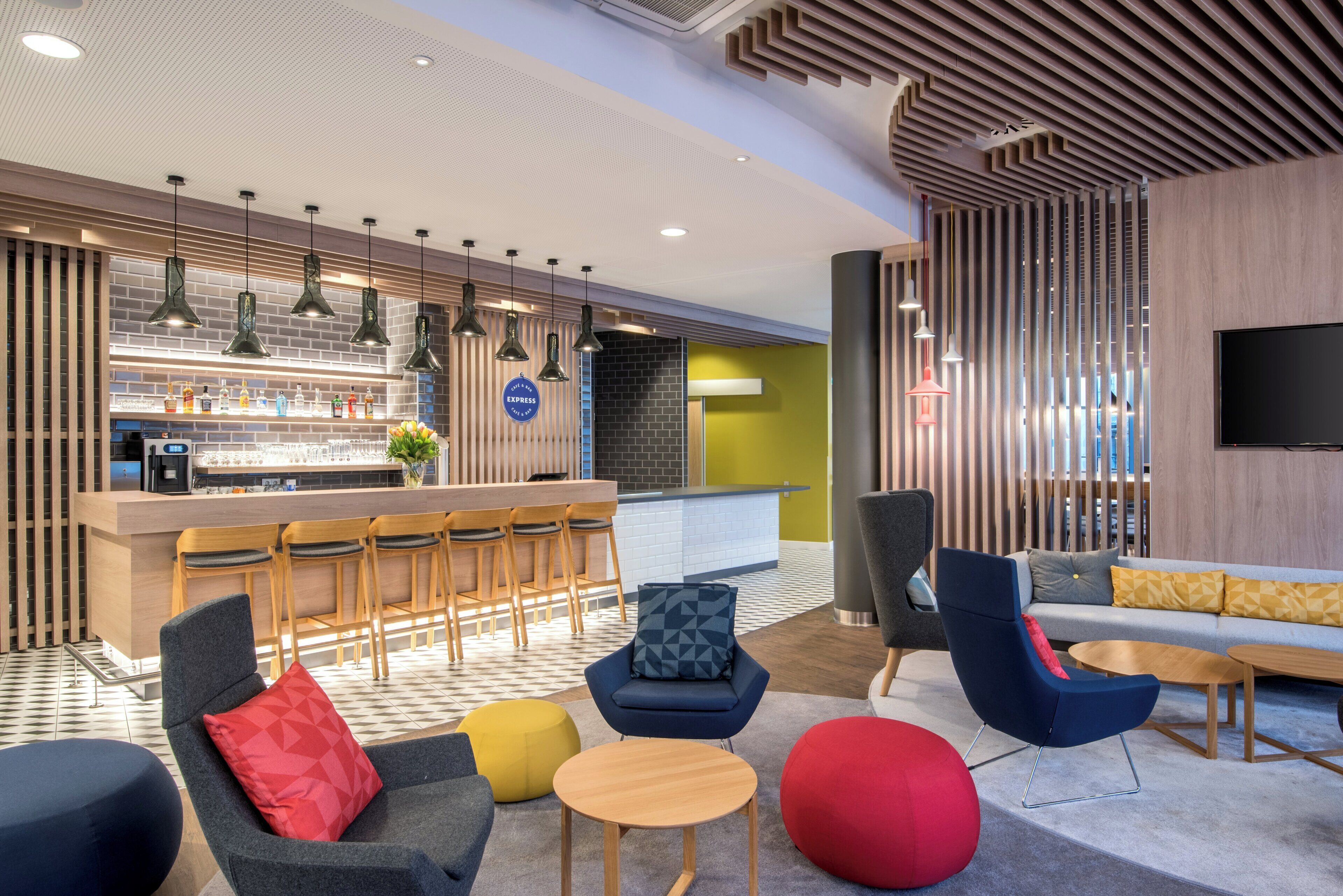 Un área de bar moderna con mostrador, taburetes, iluminación colgante y un espacio de estar con sofás y otomanas.