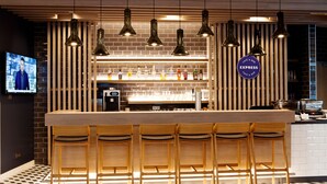Zona de bar con taburetes de madera, iluminación colgante y un cartel visible que dice 'EXPRESS Cafe & Bar'.
