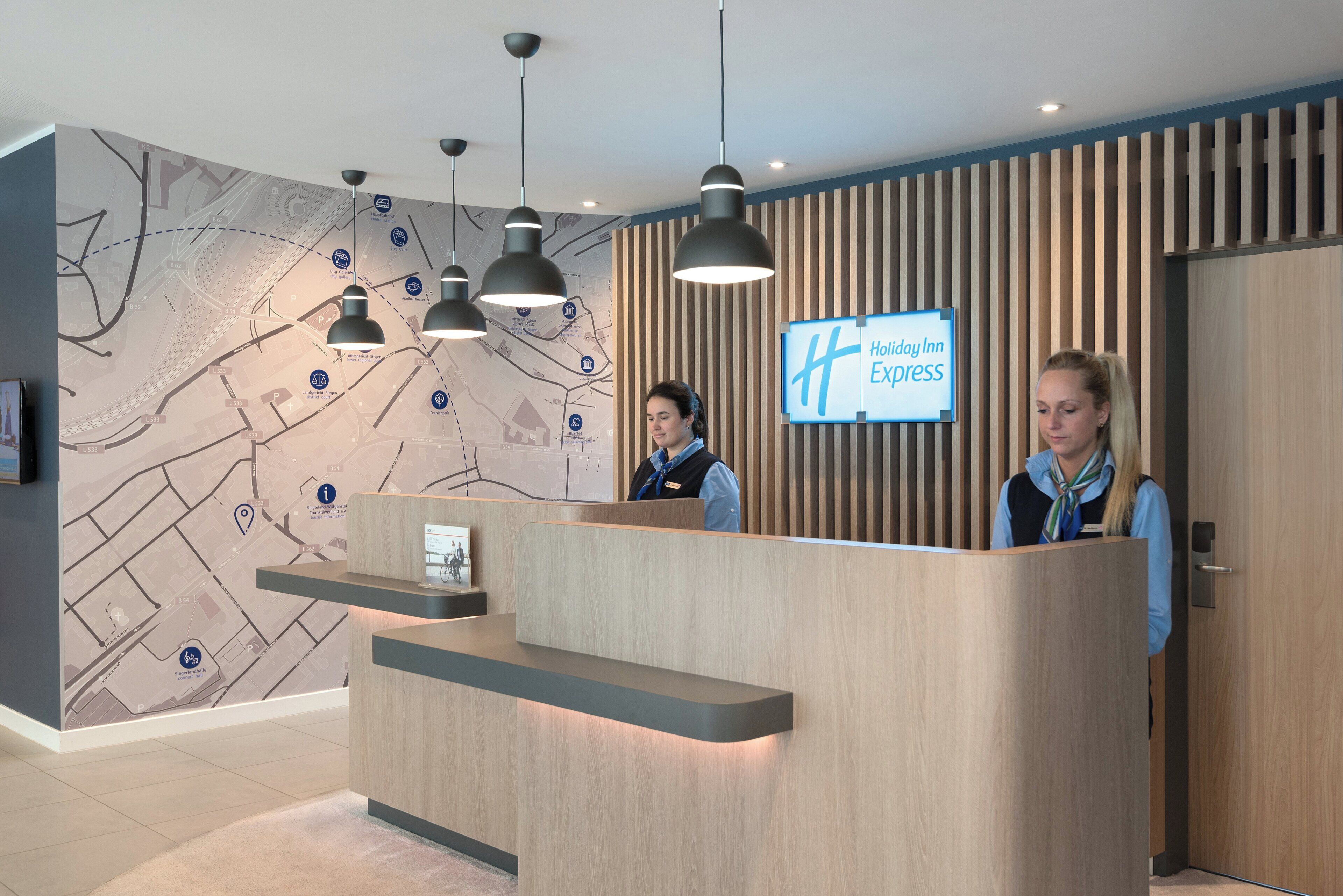 A hotel reception desk with a digital display, wooden paneling, and pendant lighting.