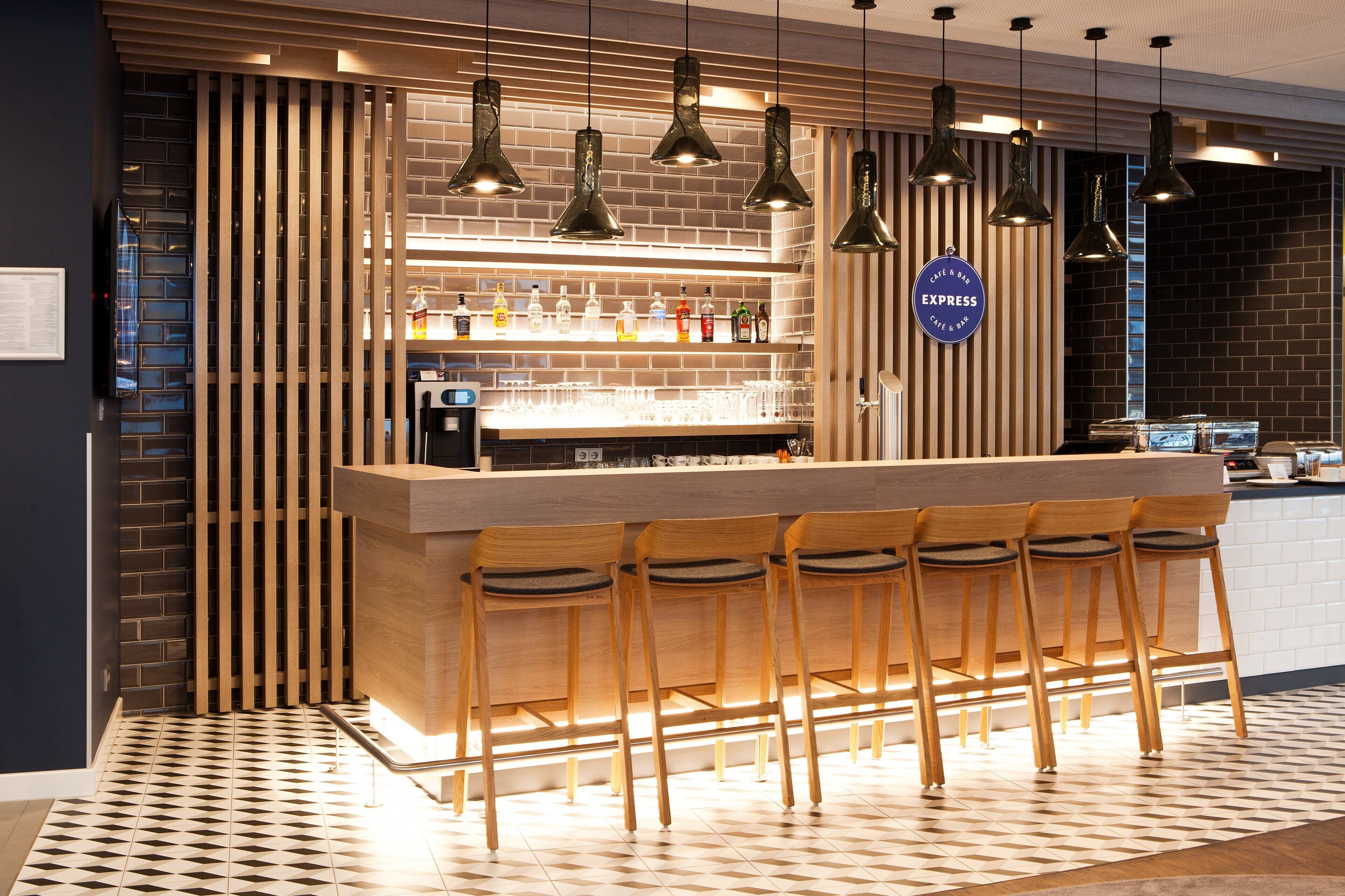 Una zona de bar con una barra larga, varias lámparas colgantes y un conjunto de taburetes.