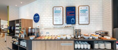 A breakfast buffet area with various food options and a coffee station.