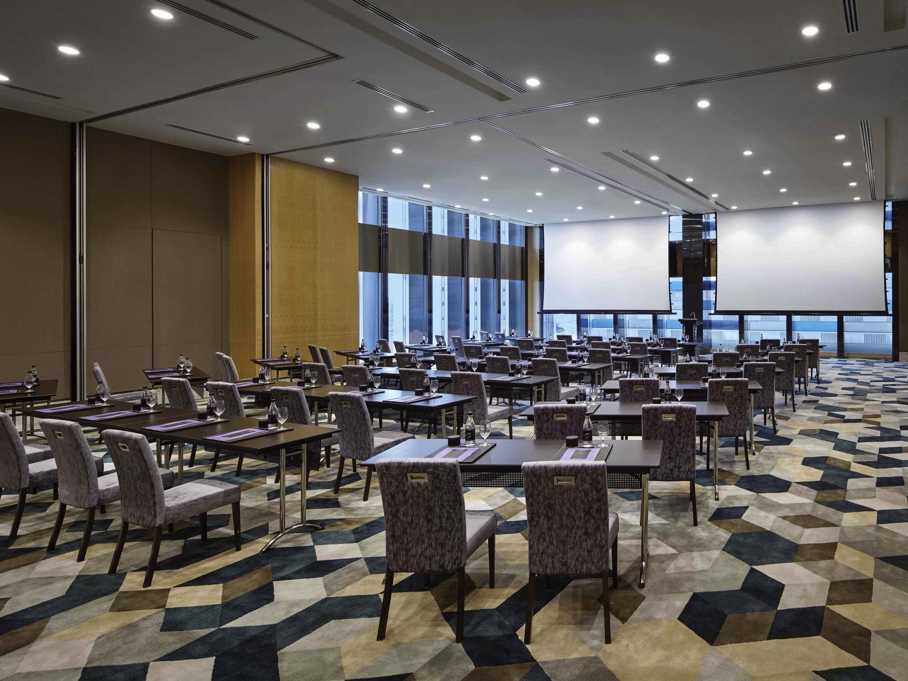 A conference room with tables, chairs, a projector screen, and large windows.