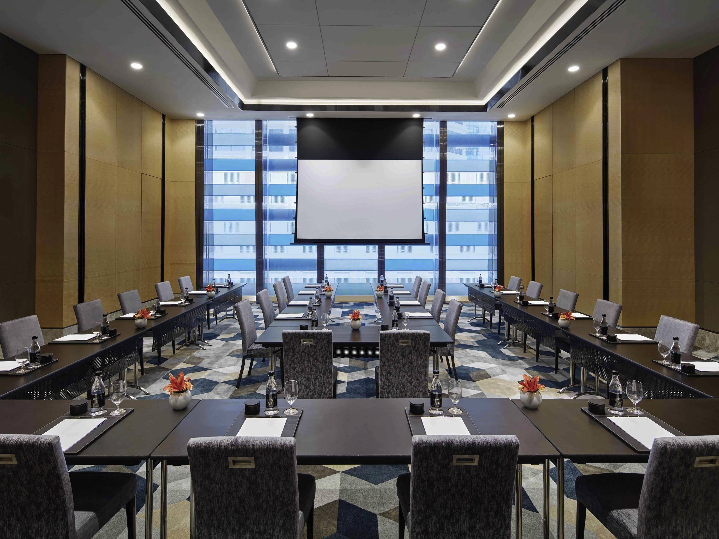 A conference room with multiple tables, chairs, and a large screen for presentations.