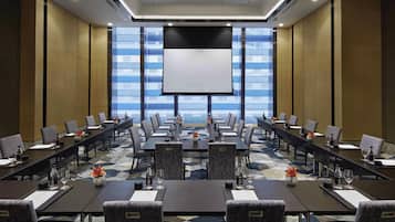 A conference room with multiple tables, chairs, and a large screen for presentations.