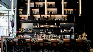 Eine Bar mit mehreren Regalen, die Flaschen und Gläser zeigen, Barhocker und einer Marmorplatte.