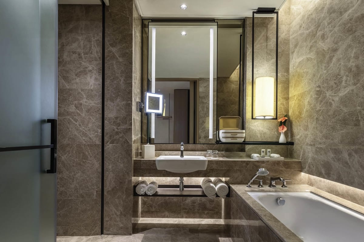 Ein modernes Badezimmer mit großem Spiegel, Badewanne, Waschbecken und einem Waschtisch mit Handtuchhalter.