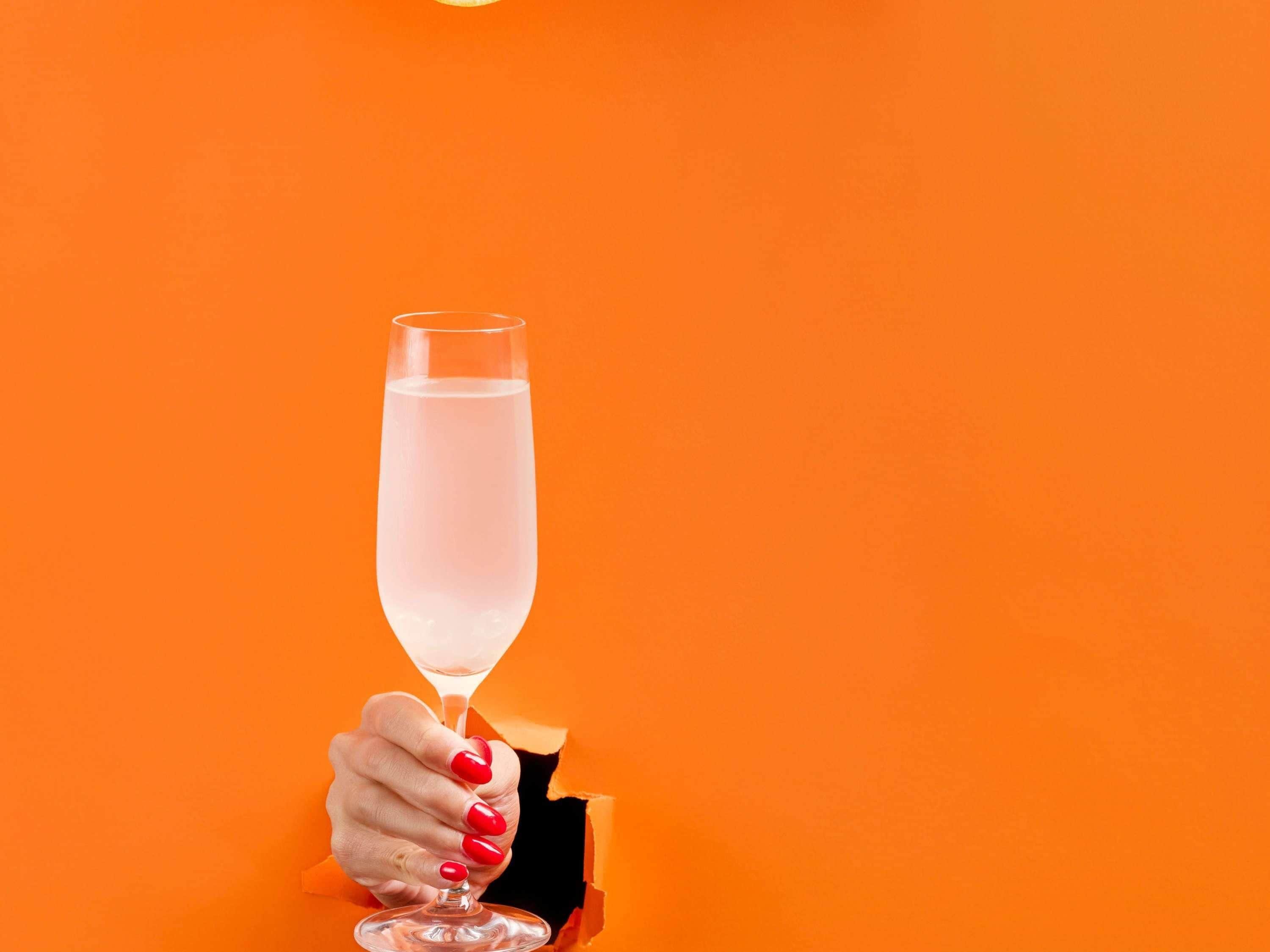 Una mano sosteniendo una copa de champán sobre un fondo naranja.