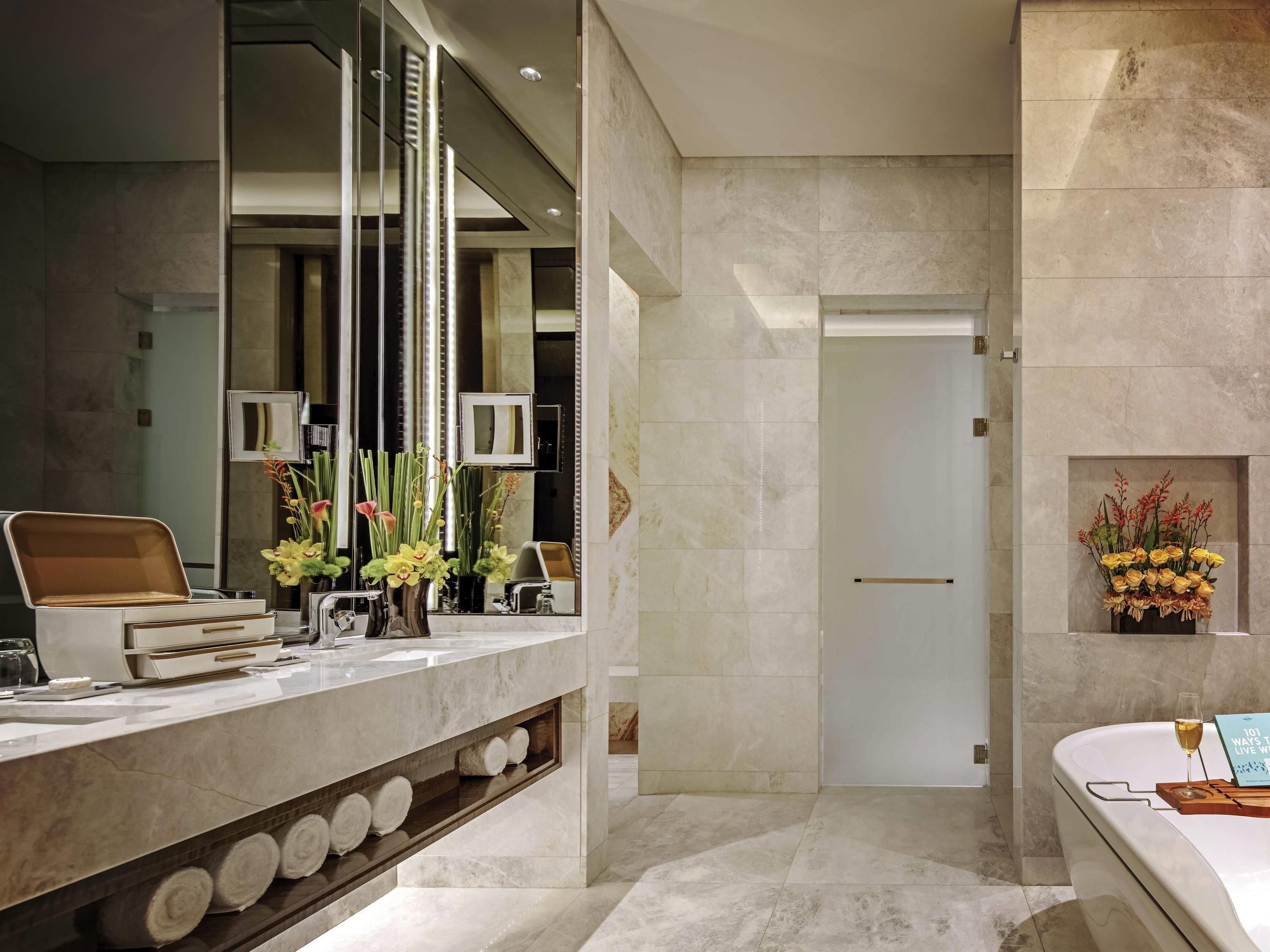A modern bathroom with a marble countertop, a mirror, a towel rack, and a vase with flowers.
