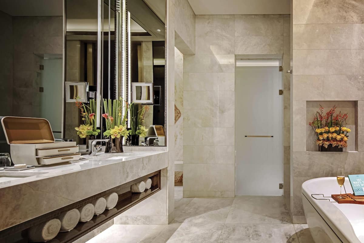 A modern bathroom with a marble countertop, a mirror, a towel rack, and a vase with flowers.