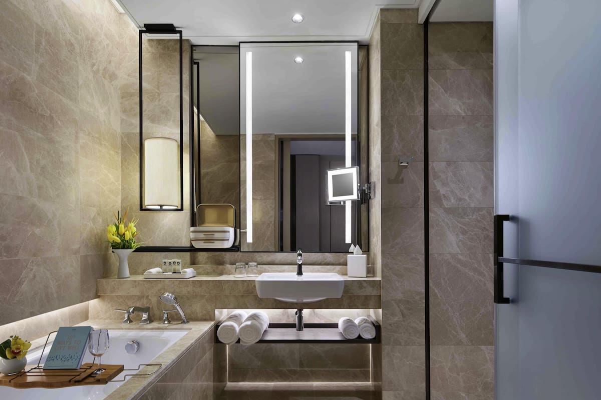 A modern bathroom with a large mirror, a bathtub, and a vanity with a sink.