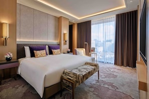 A modern hotel room with a large bed, a bench, a nightstand, a lamp, and a view of the city. - Sofitel Singapore City Centre (Singapore)