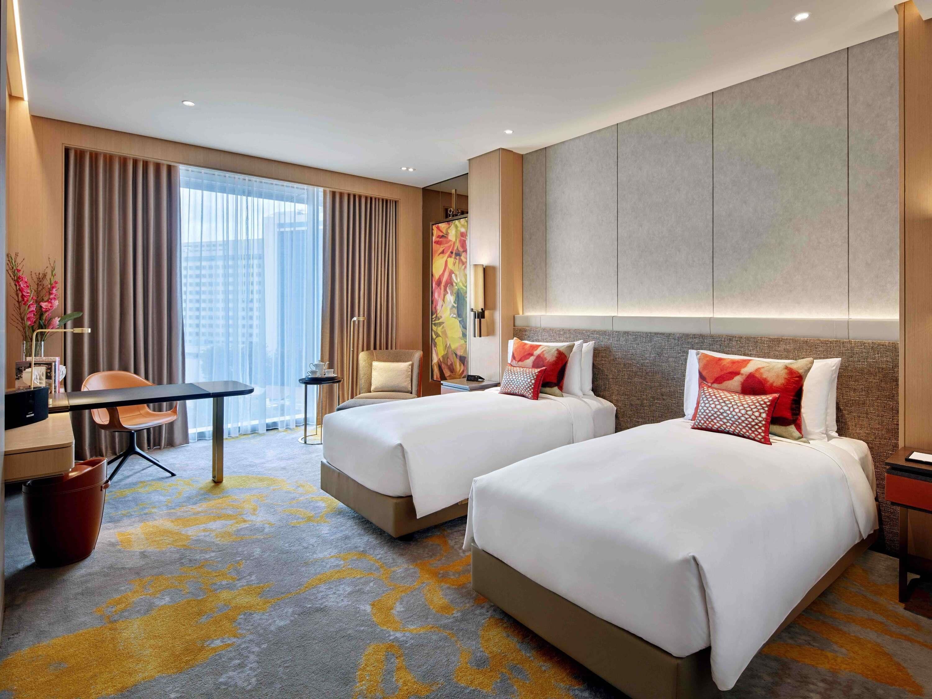A hotel room with two beds, a desk, a chair, and a large window with curtains.