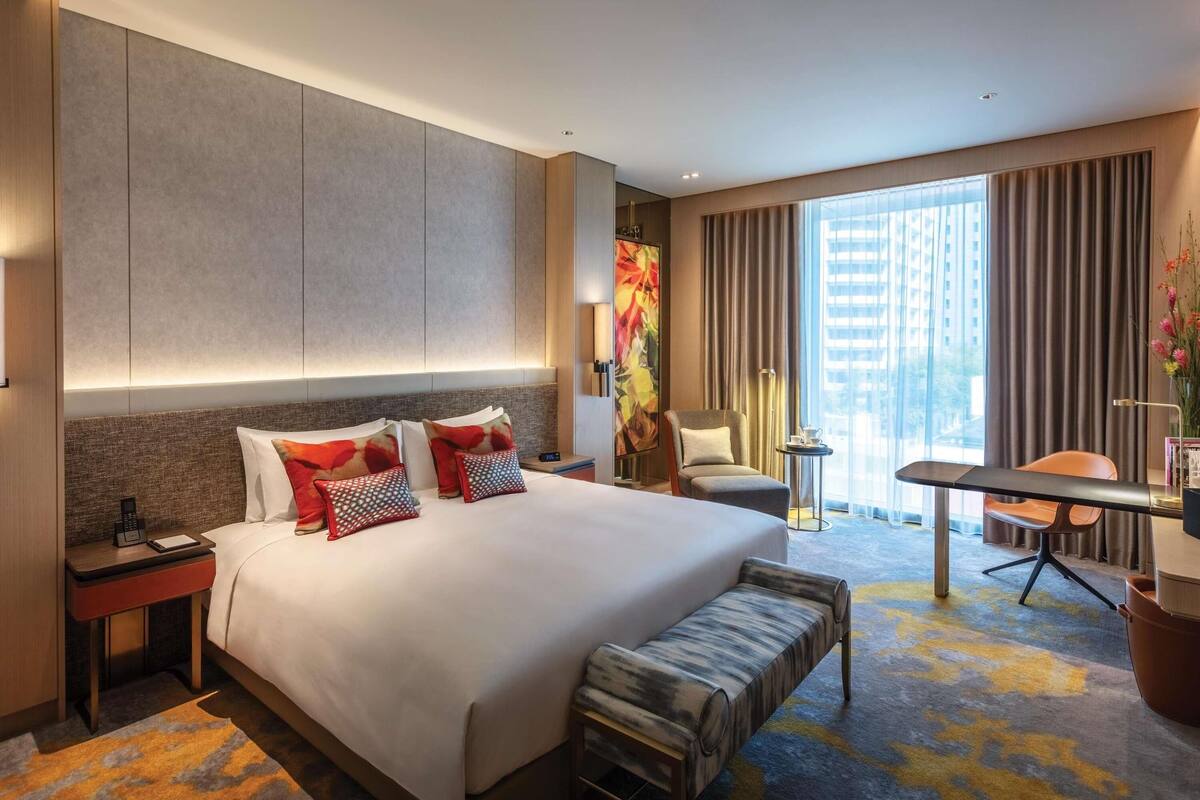 Ein modernes Hotelzimmer mit einem großen Bett, Nachttischen, einem Schreibtisch, einem Sessel und Blick auf die Stadt.