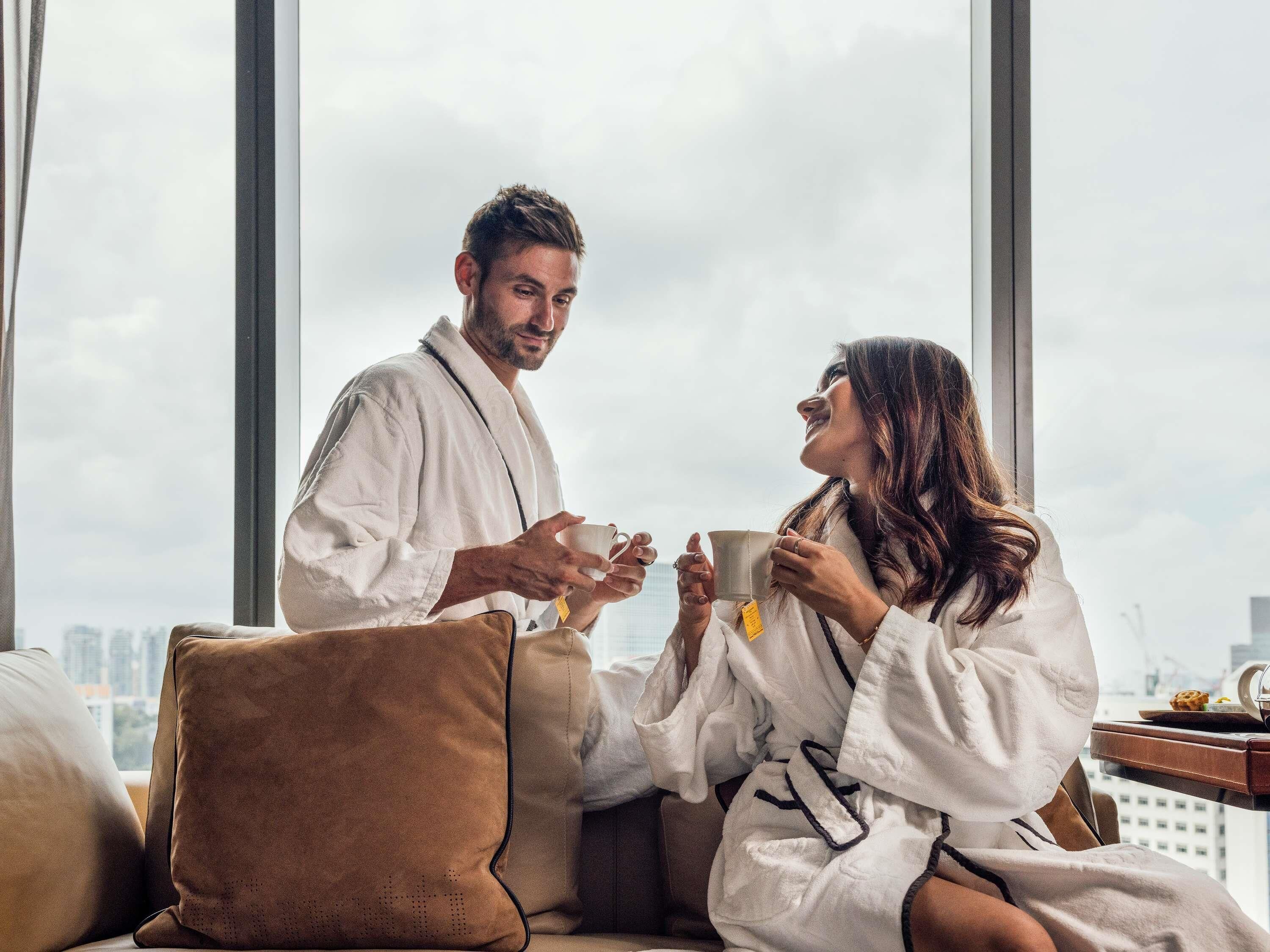 A couple in a robe sitting by a window with a city view.