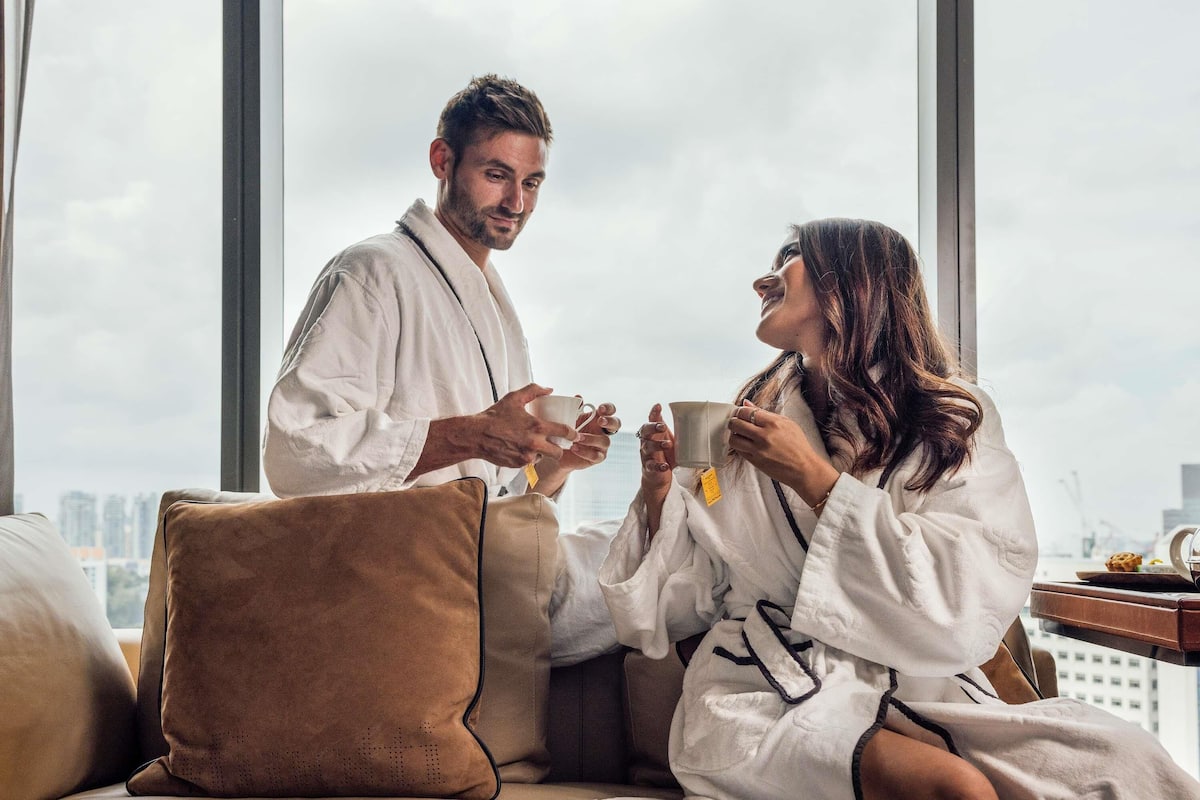 A couple in a robe sitting by a window with a city view.