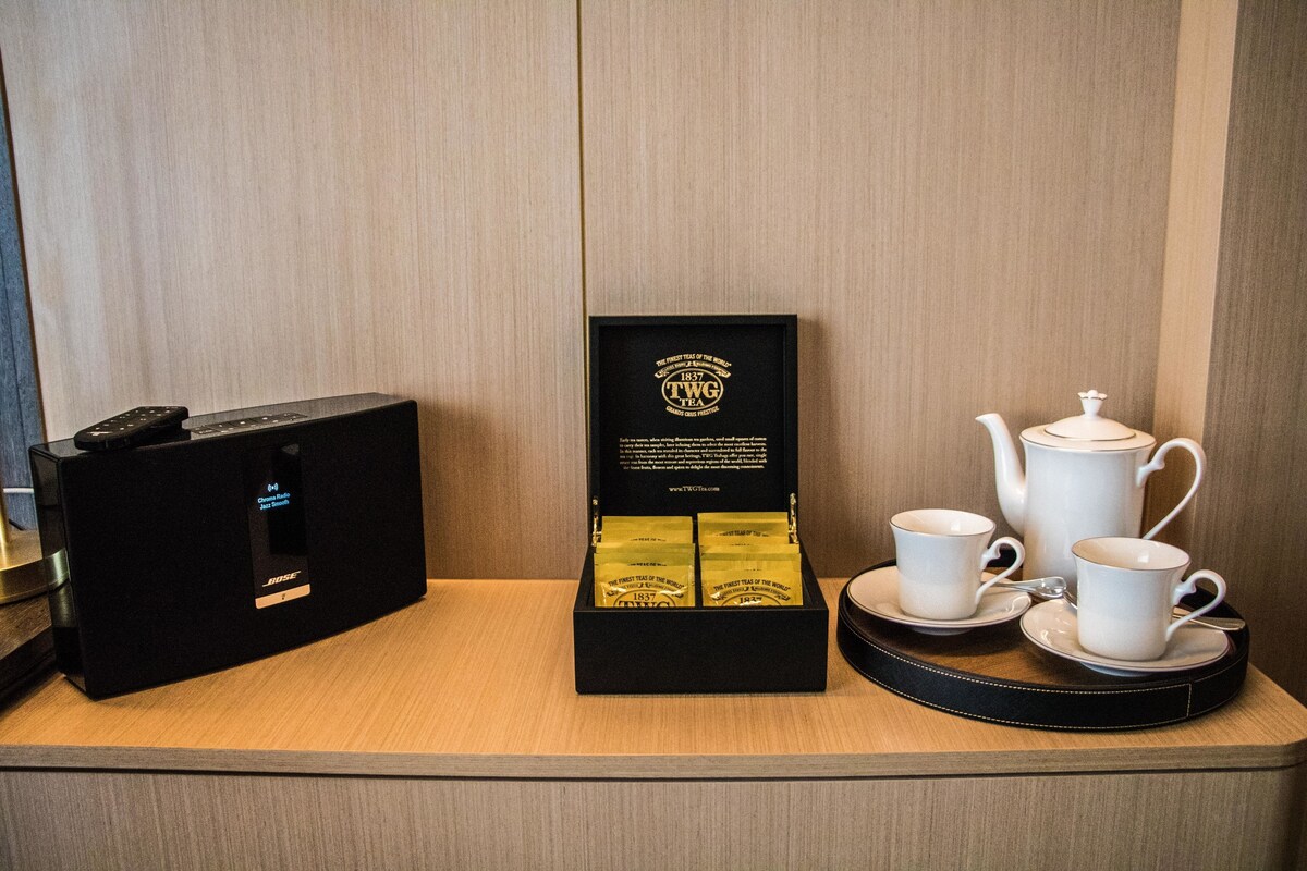 A black audio system, a box of TWG tea, and a tea set on a wooden table.