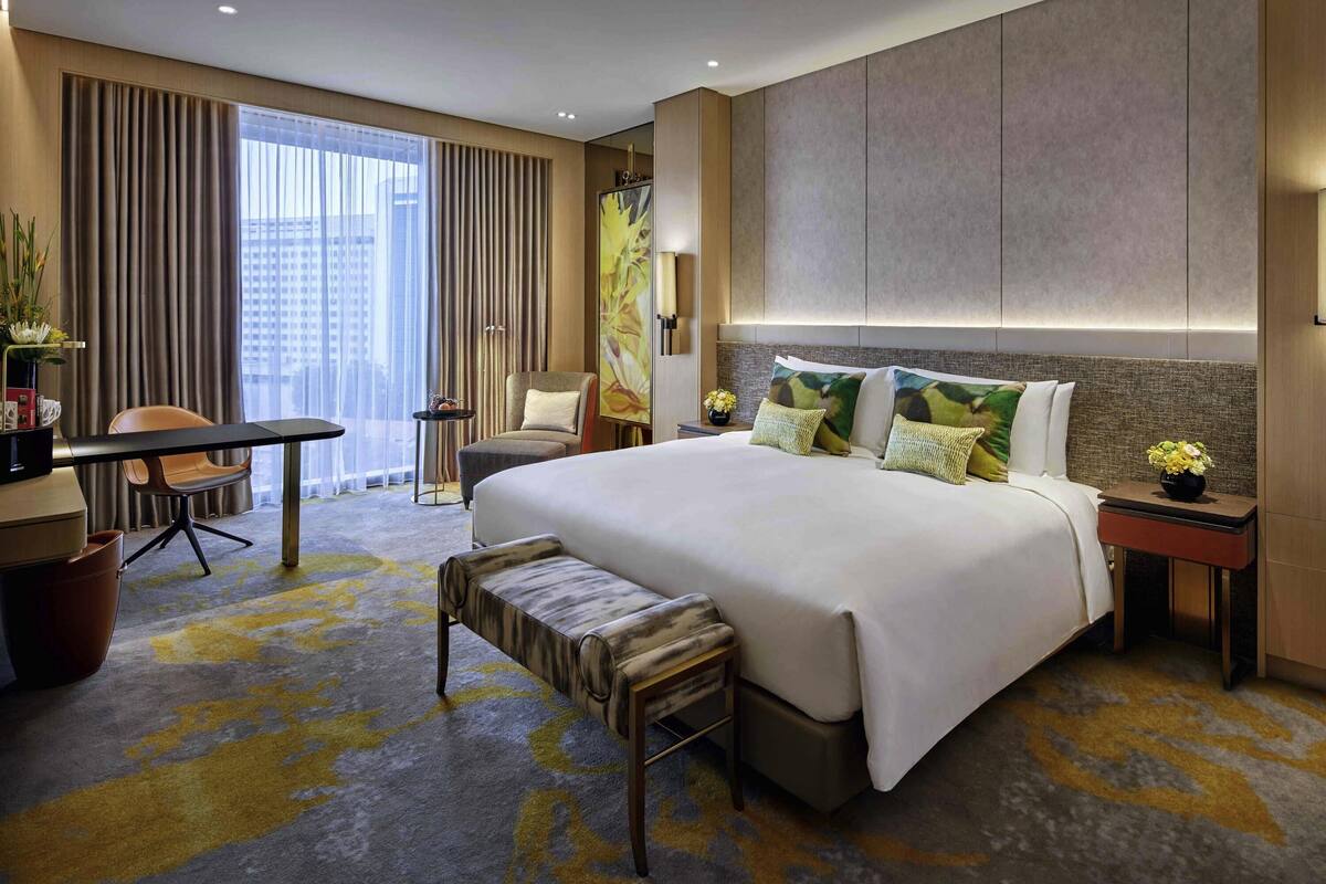 Ein Hotelzimmer mit einem großen Bett, einem Schreibtisch, einem Stuhl, einer Bank und Blick auf die Stadt.
