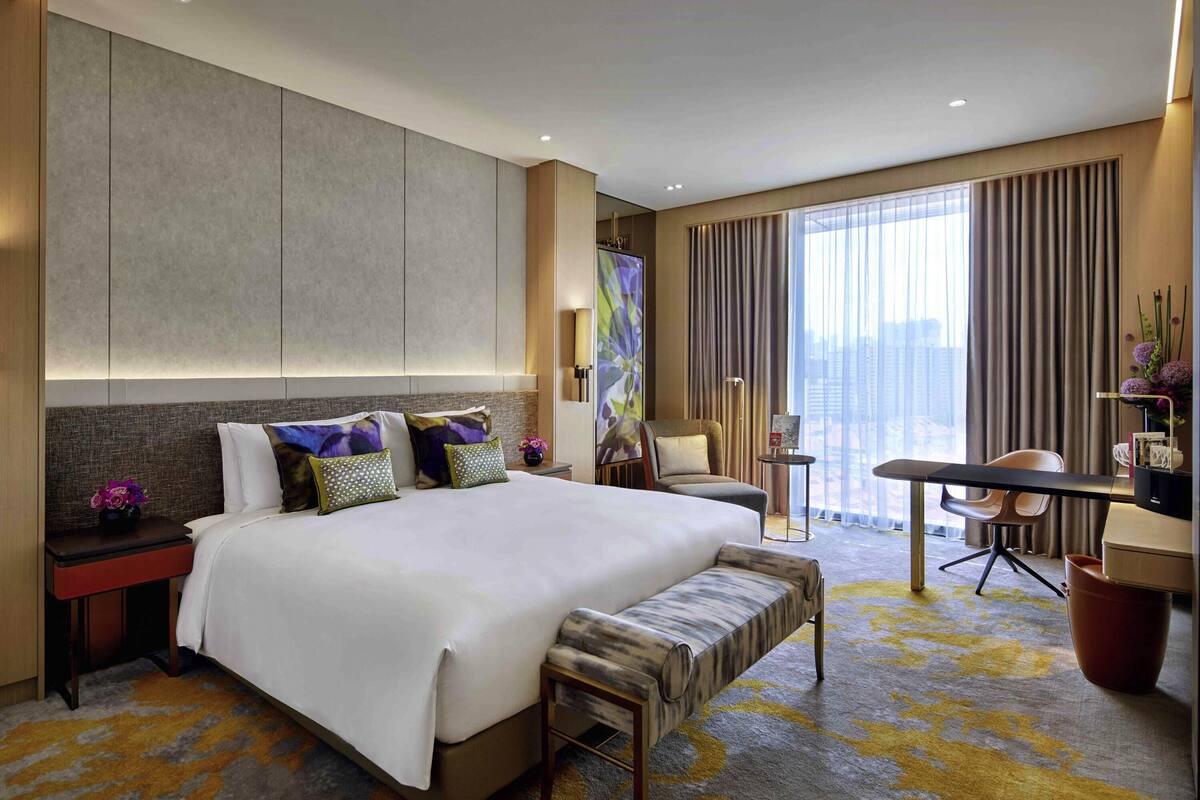 Ein Hotelzimmer mit einem großen Bett, einem Schreibtisch, einem Stuhl und Blick auf die Stadt.
