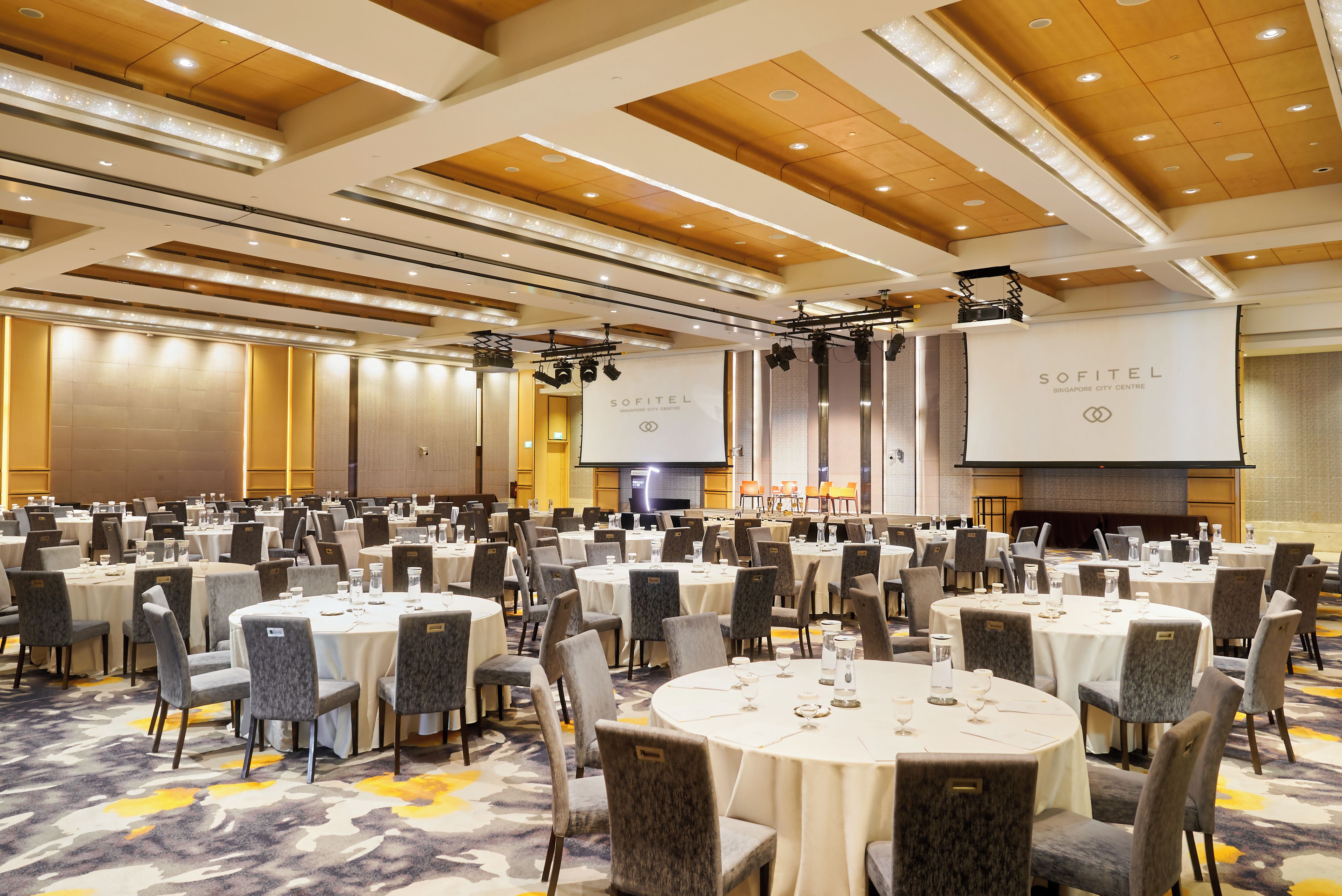 A conference room with multiple round tables, chairs, and a stage with a screen.