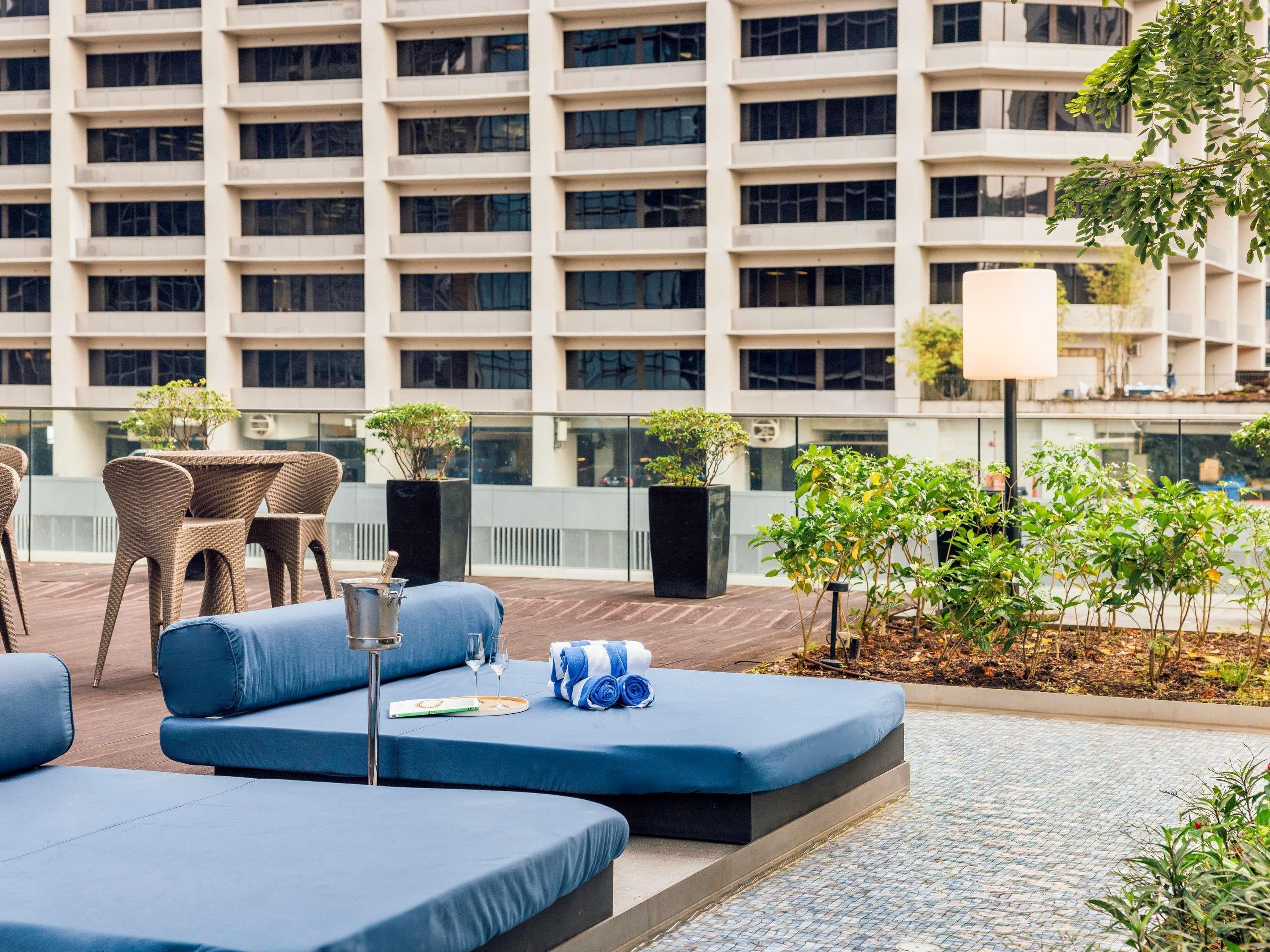 A rooftop lounge area with blue seating, a table with chairs, and potted plants.