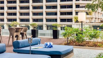 A rooftop lounge area with blue seating, a table with chairs, and potted plants.