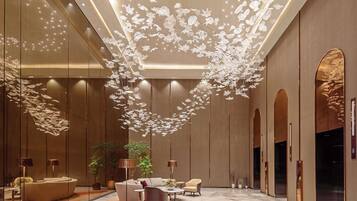 A modern lobby with a central seating area, a decorative ceiling installation, and a large mirror.