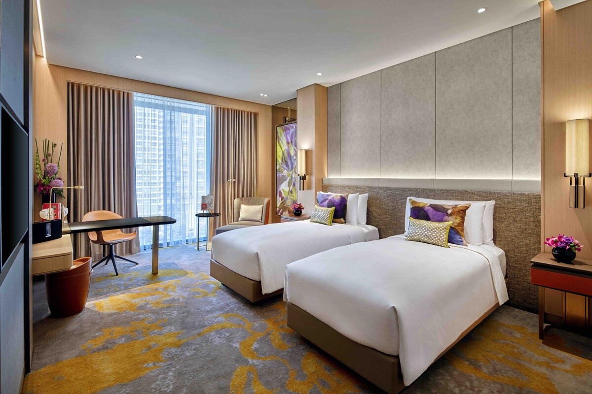 A hotel room with two beds, a desk, a chair, and a large window.