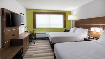 A hotel room with two beds, a desk, a flat-screen TV, a window, and a lamp.