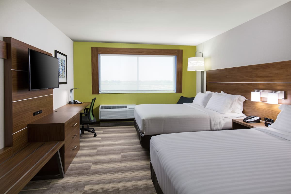 A hotel room with two beds, a desk with a flat-screen TV, a window with a view, and a lamp.