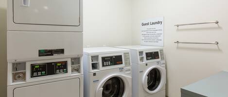 A laundry area with stacked washers and dryers, a sign for guest laundry, and metal towel racks on the wall.