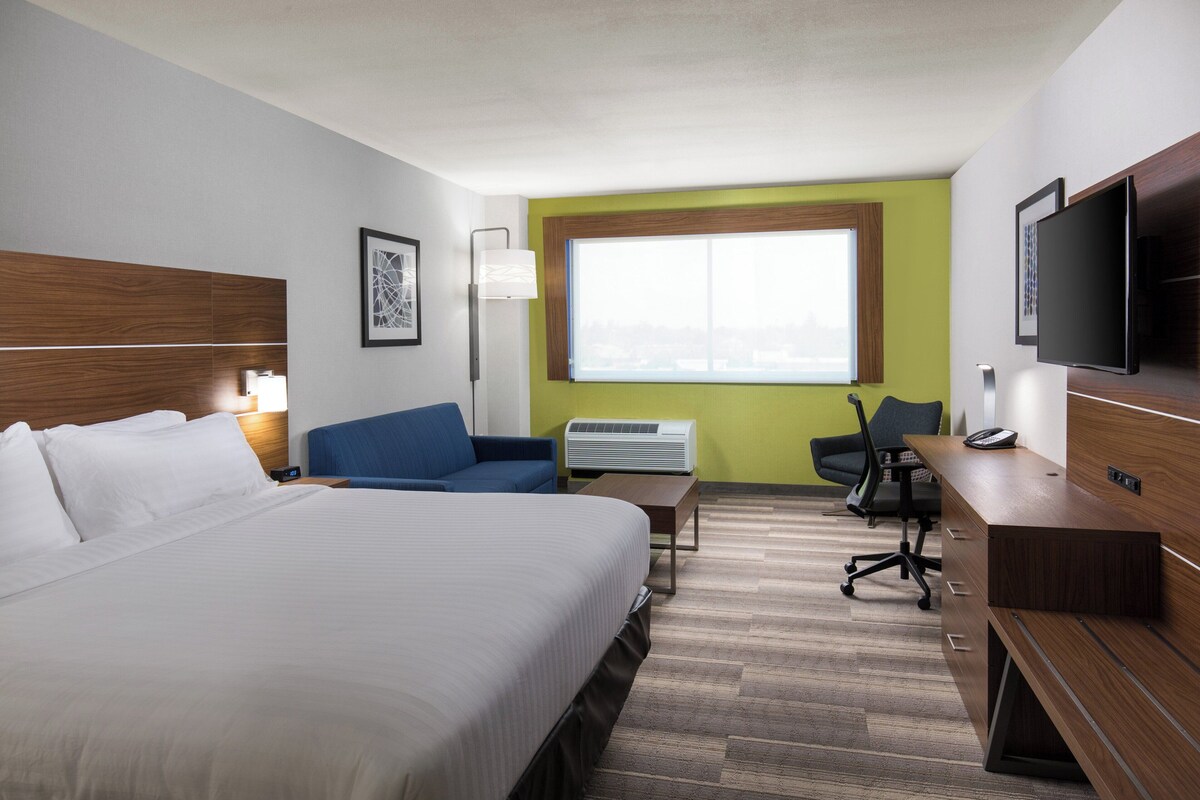 A hotel room with a bed, a desk, a chair, a television, and a window.