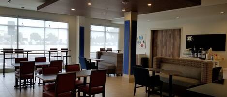 A spacious indoor area with tables and chairs, large windows, and a modern ceiling design.