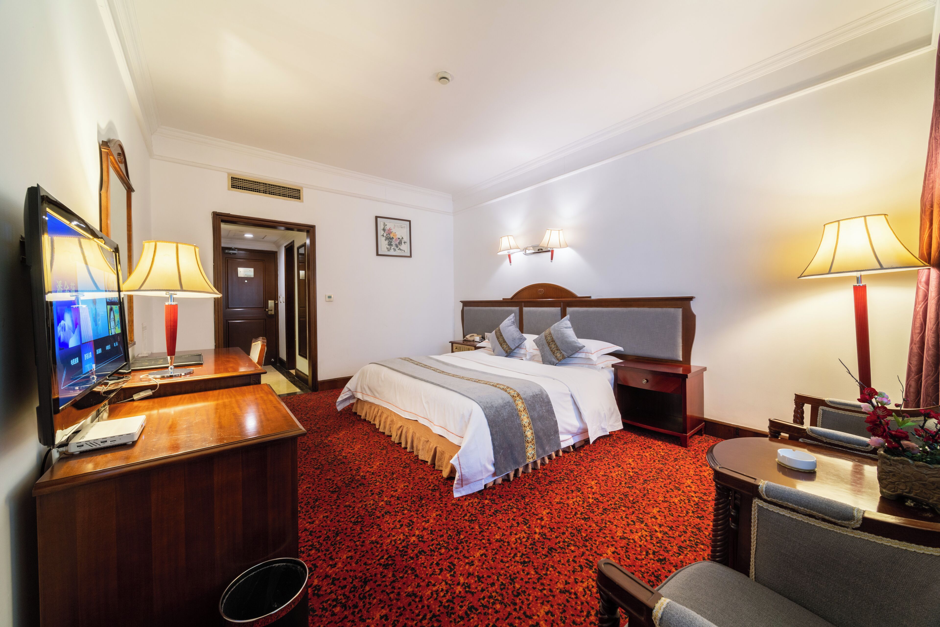 Una habitación de hotel con cama, escritorio, televisión y lámparas.