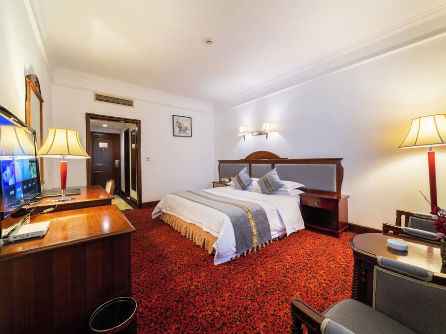 A hotel room with a bed, desk, television, and lamps.