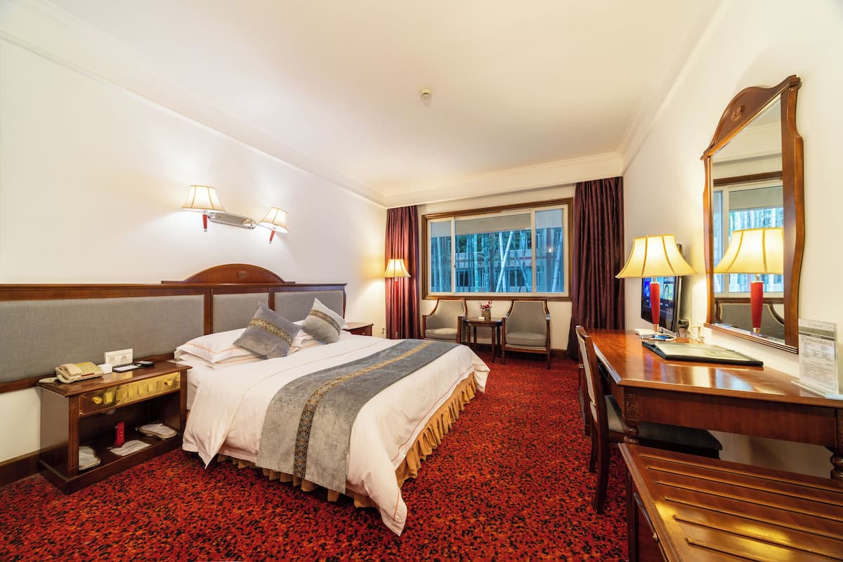 A hotel room with a large bed, a desk, a chair, a small table, and a window with curtains.
