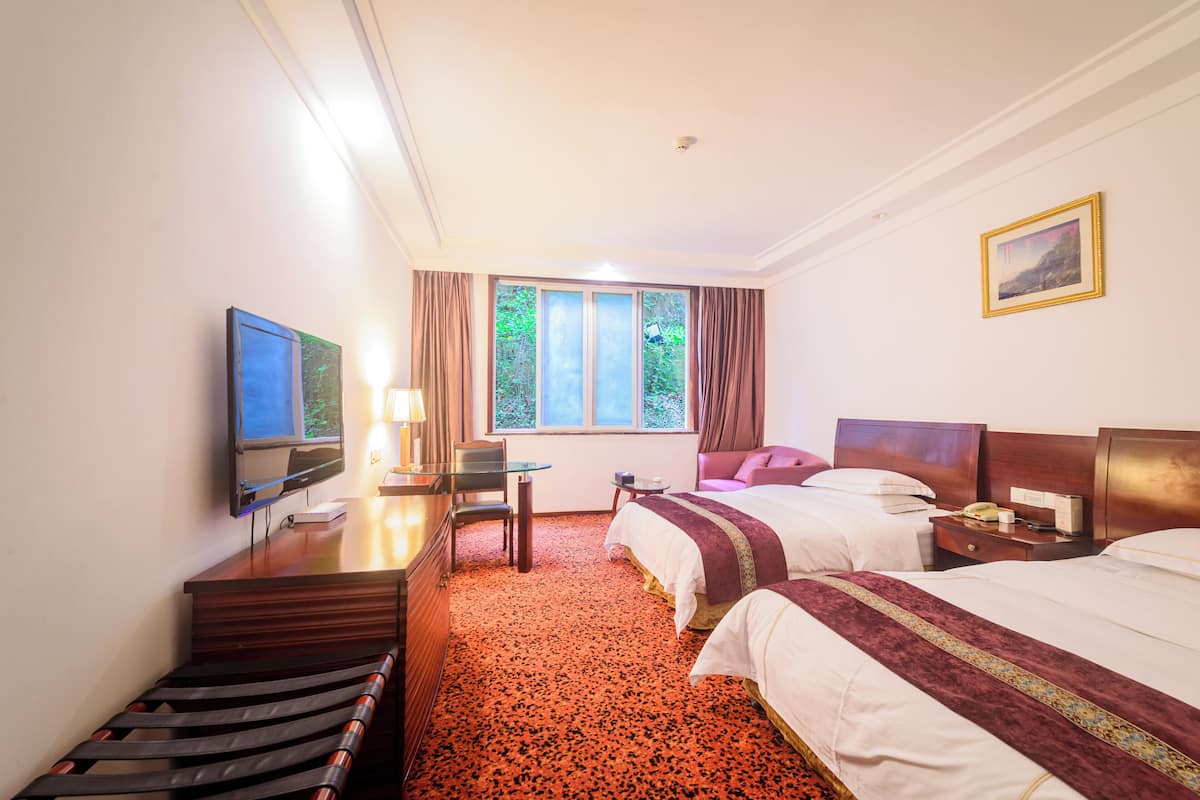 A hotel room with two beds, a desk, a television, and a window with curtains.