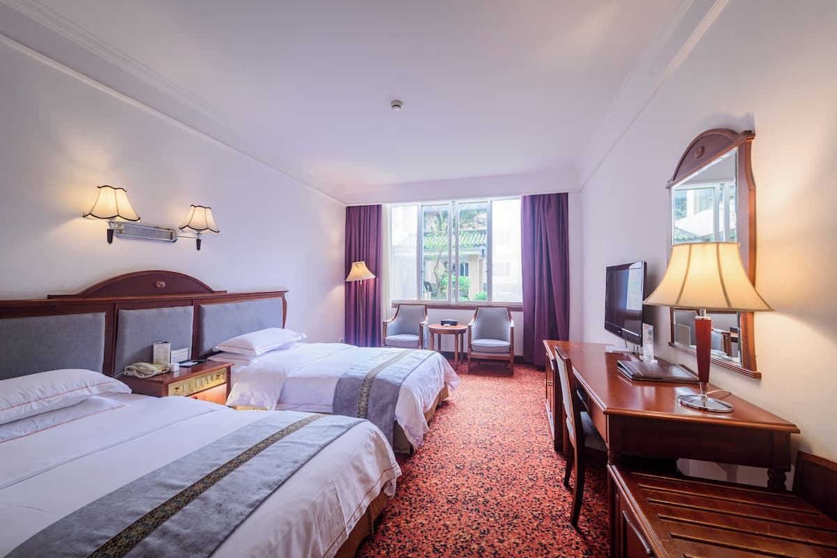 A hotel room with two beds, a desk, a chair, a TV, and a window with curtains.
