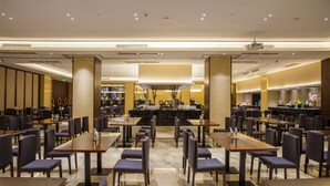 Un restaurante espacioso con numerosas mesas y sillas, una zona de bar central y una decoración de diseño moderno.