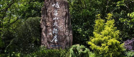Ein großer Felsen mit eingekerbtem Text, umgeben von üppigem Grün und einem kleinen Baum.