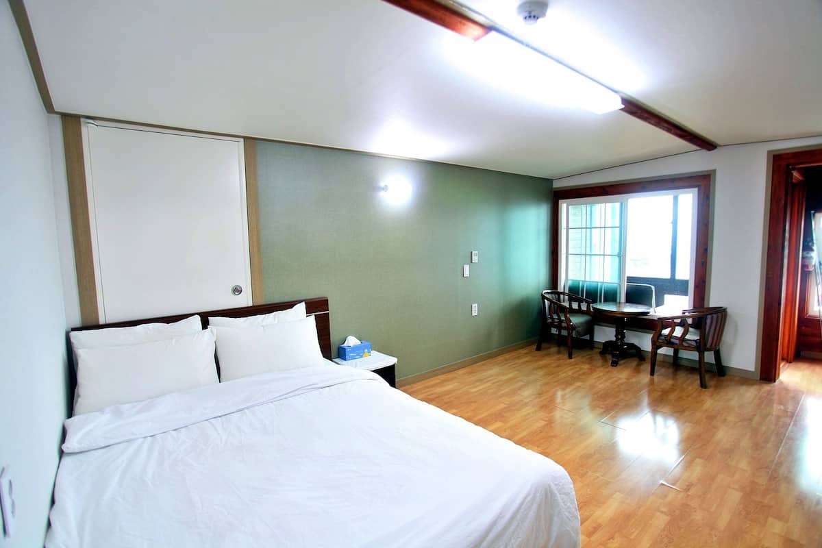 Une chambre d’hôtel avec un lit, un bureau avec des chaises, une fenêtre et une porte.